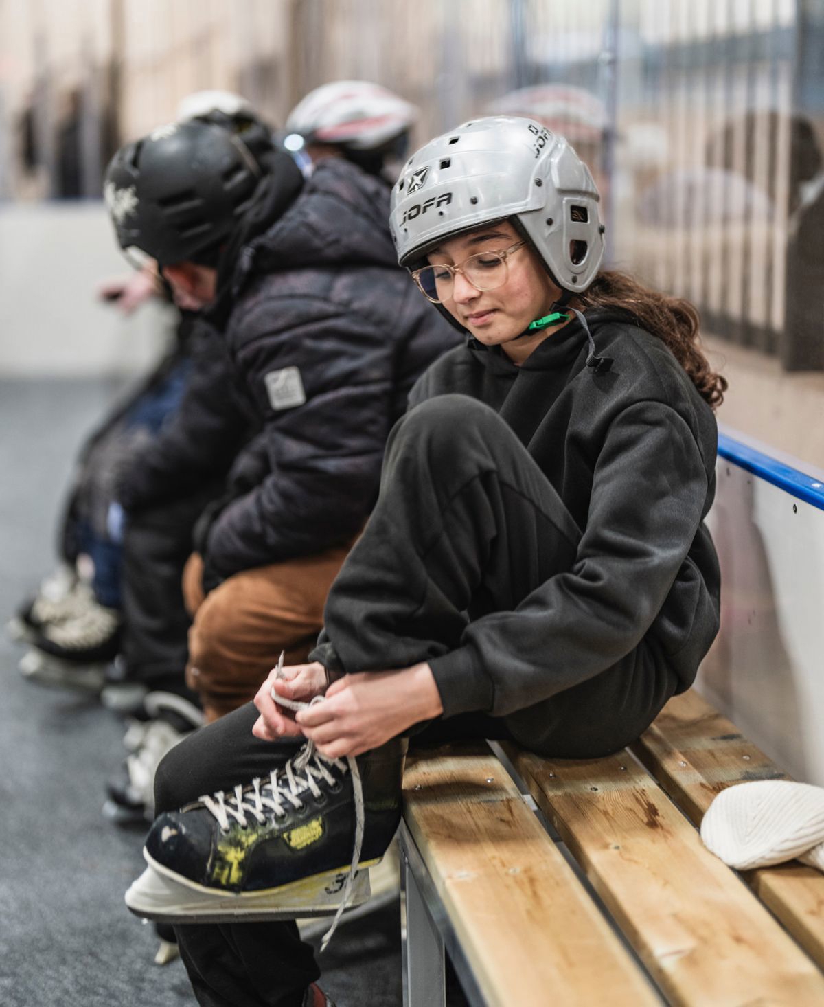 En flicka sitter på en bänk i en ishall och snörar skridskor.