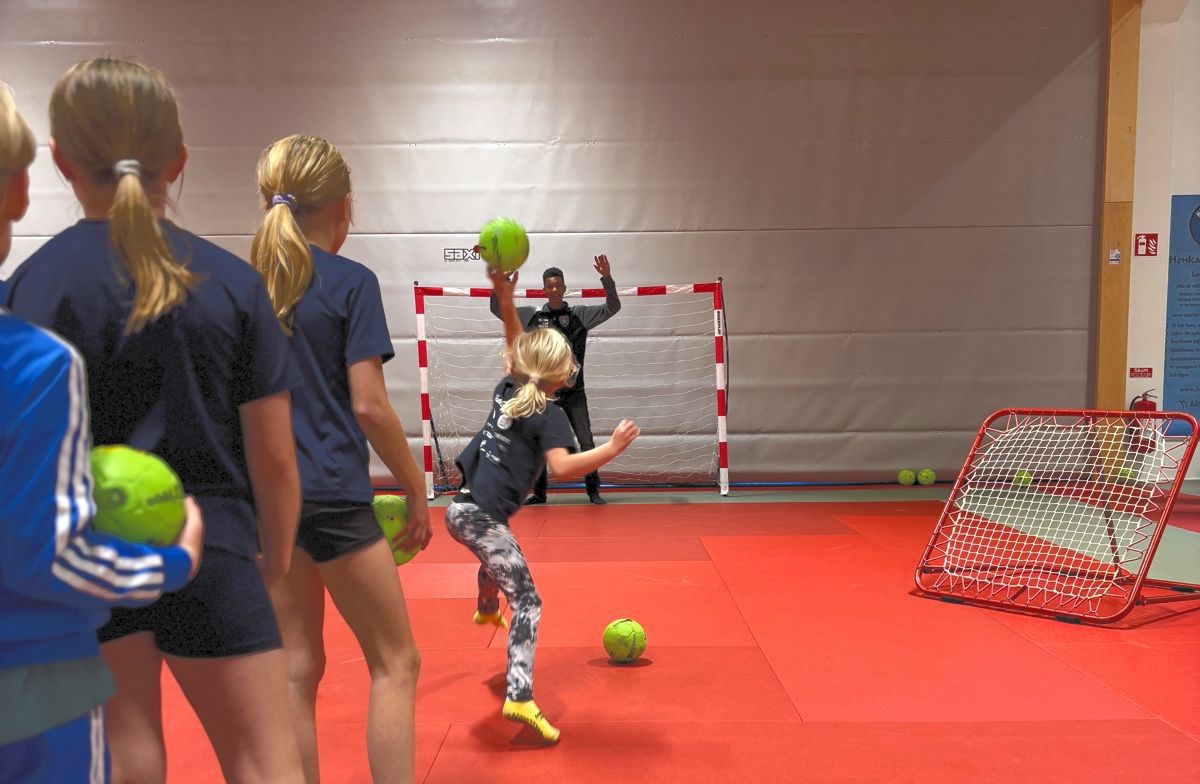 Barn står i kö och ska kast handboll i mål. Målvakt finns i målet.