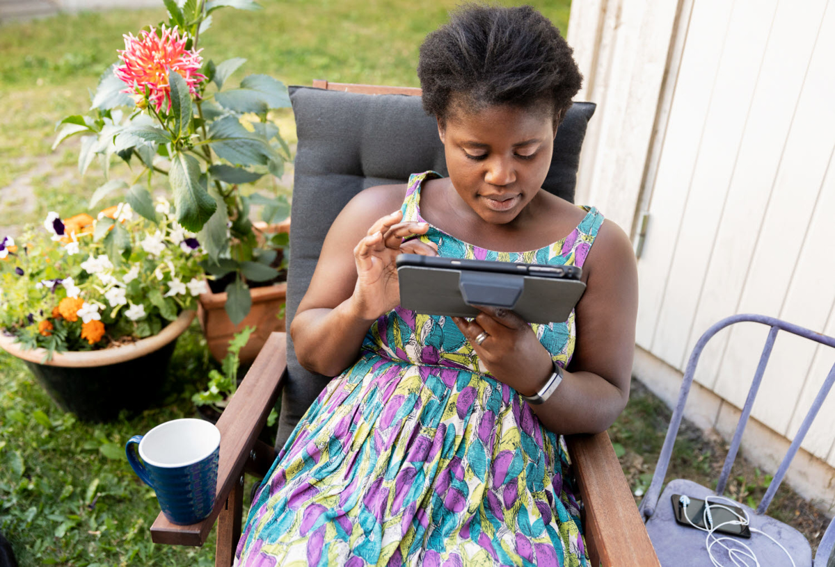 En kvinna sitter i trädgården med en iPad