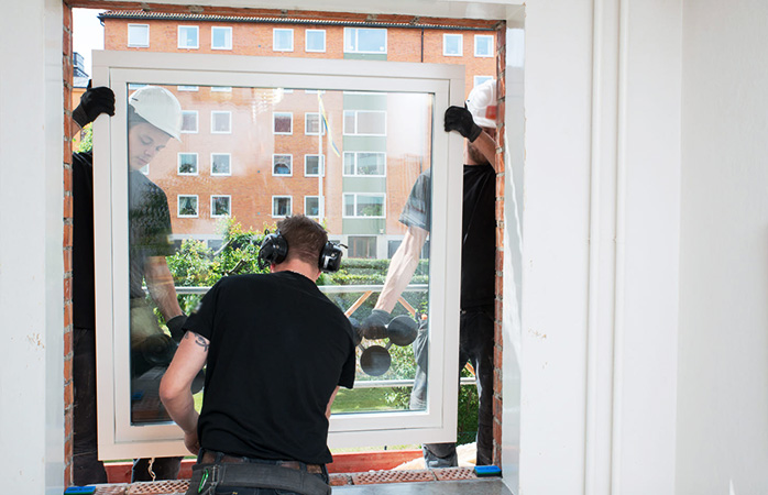 Tre personer monterar fönster i en lägenhet.