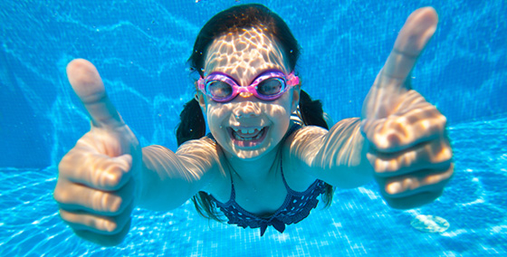 Flicka simmar under vattnet i en pool