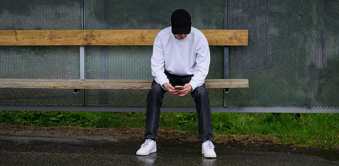 Ung kille med mobiltelefon sitter ensam på en parkbänk.